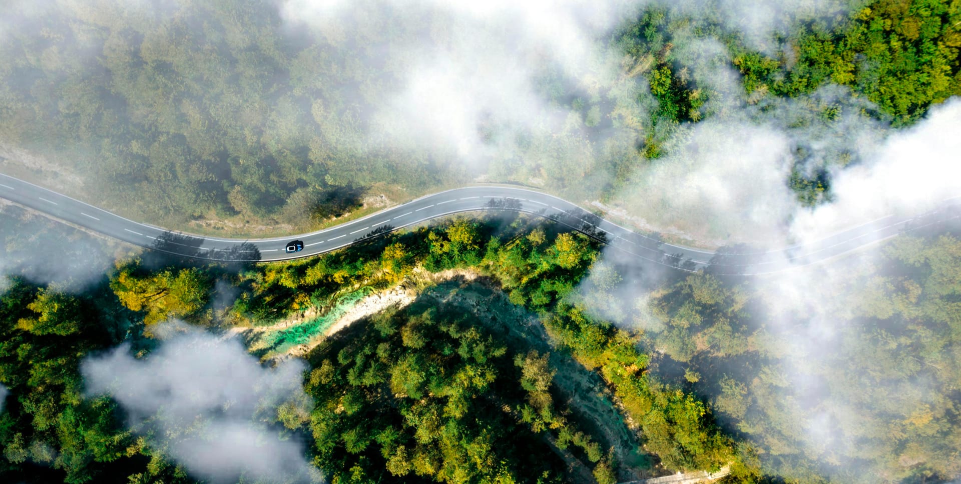 Vista aérea de um carro atravessando montanhas cobertas de florestas envoltas em névoa, simbolizando a missão de geração de energia limpa da Solavita e seu compromisso com soluções sustentáveis e ecológicas