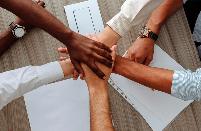 Diversas mãos unidas sobre uma mesa, simbolizando trabalho em equipe, unidade e colaboração, representando o compromisso da Solavita com parcerias sólidas e esforços de vendas cooperativas